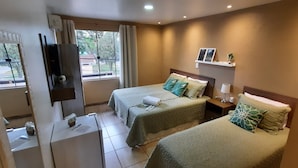 A hotel room with two beds, a small desk, a TV, a window with curtains, and a shelf with pictures. - Pousada Vó Celina (Praia Grande)