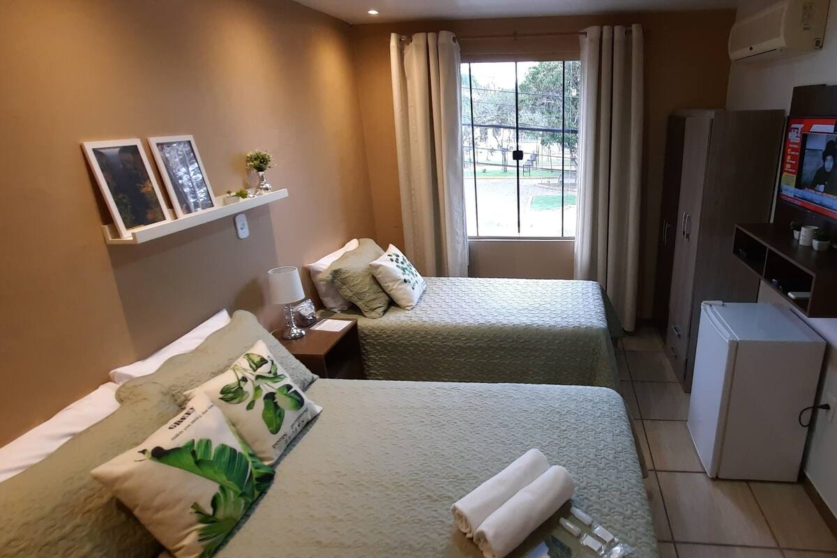 Une chambre d’hôtel avec deux lits, une télévision, un petit réfrigérateur et une fenêtre avec des rideaux.