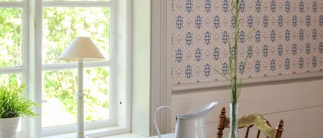 Ein Zimmer mit Fenster, Tisch mit Krug, Lampe und Topfpflanze.
