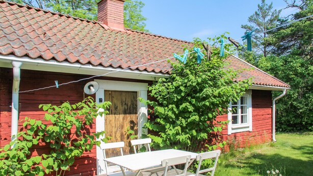 A red wooden house with a tiled roof, a white door, and a small porch with a table and chairs. - Amazing home in Gamleby (Gamleby)