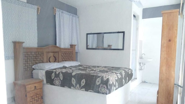 A bedroom with a bed, a wooden nightstand, a mirror, and a door. - Hotel Juarez (Cuernavaca)