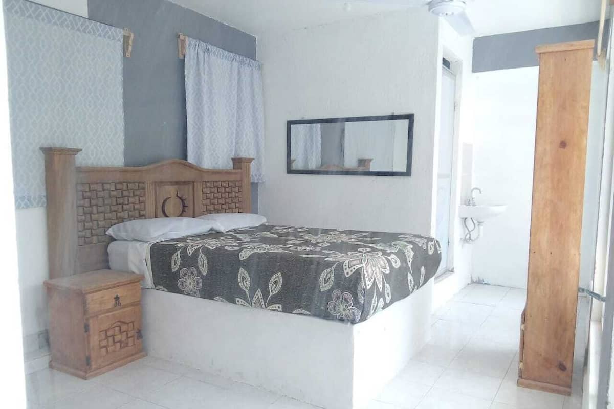Un dormitorio con una cama, una mesita de noche de madera, un espejo y una puerta.