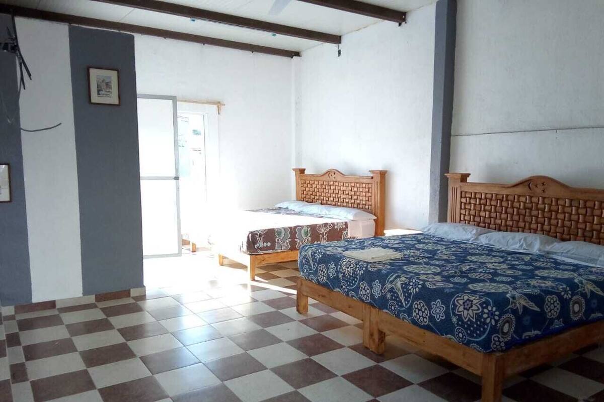 Una habitación con dos camas de madera con cabeceras, pisos de baldosas a cuadros y una puerta que da al exterior.