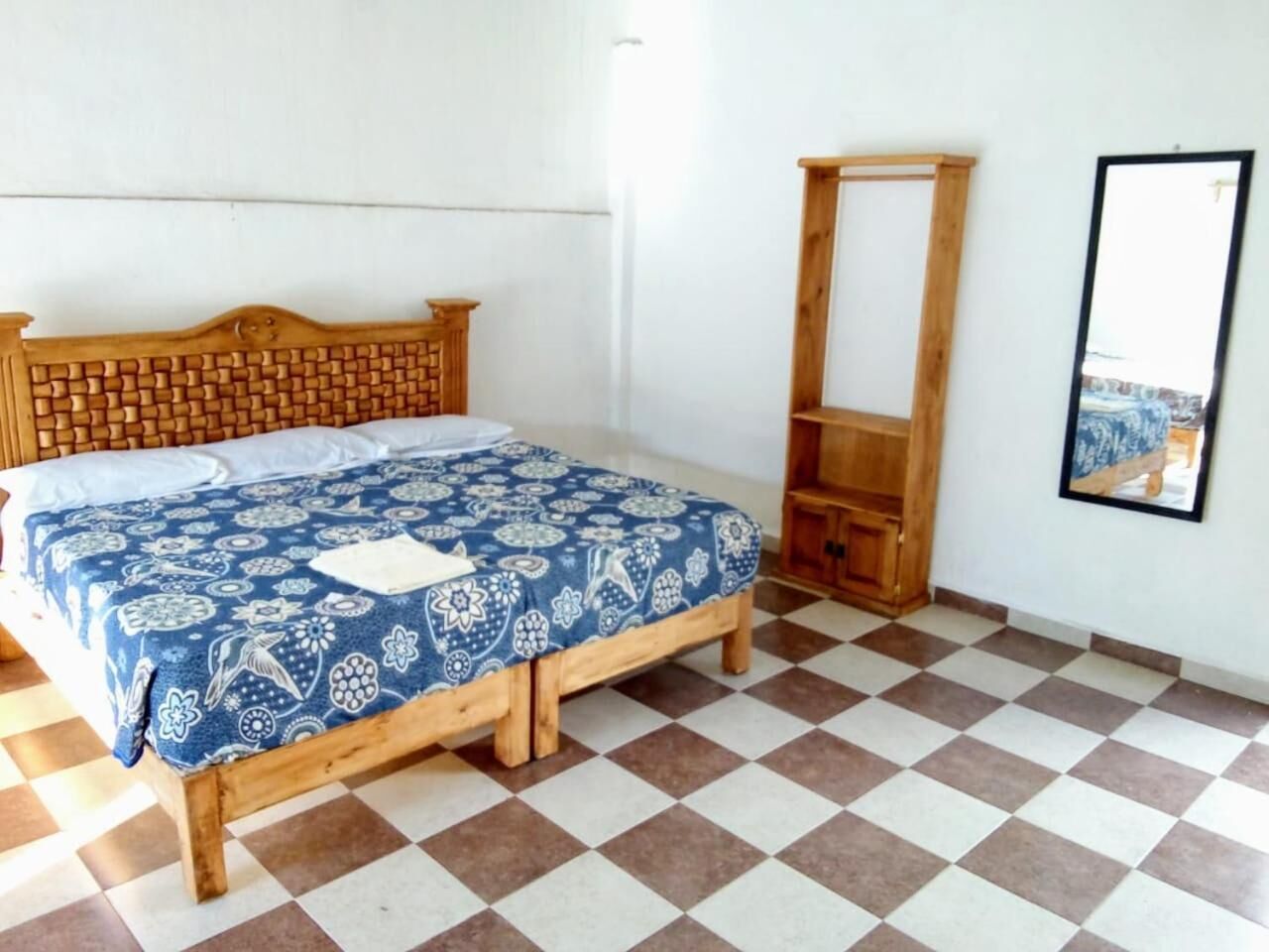 Un dormitorio con piso a cuadros, estructura de cama de madera y colcha azul estampada.