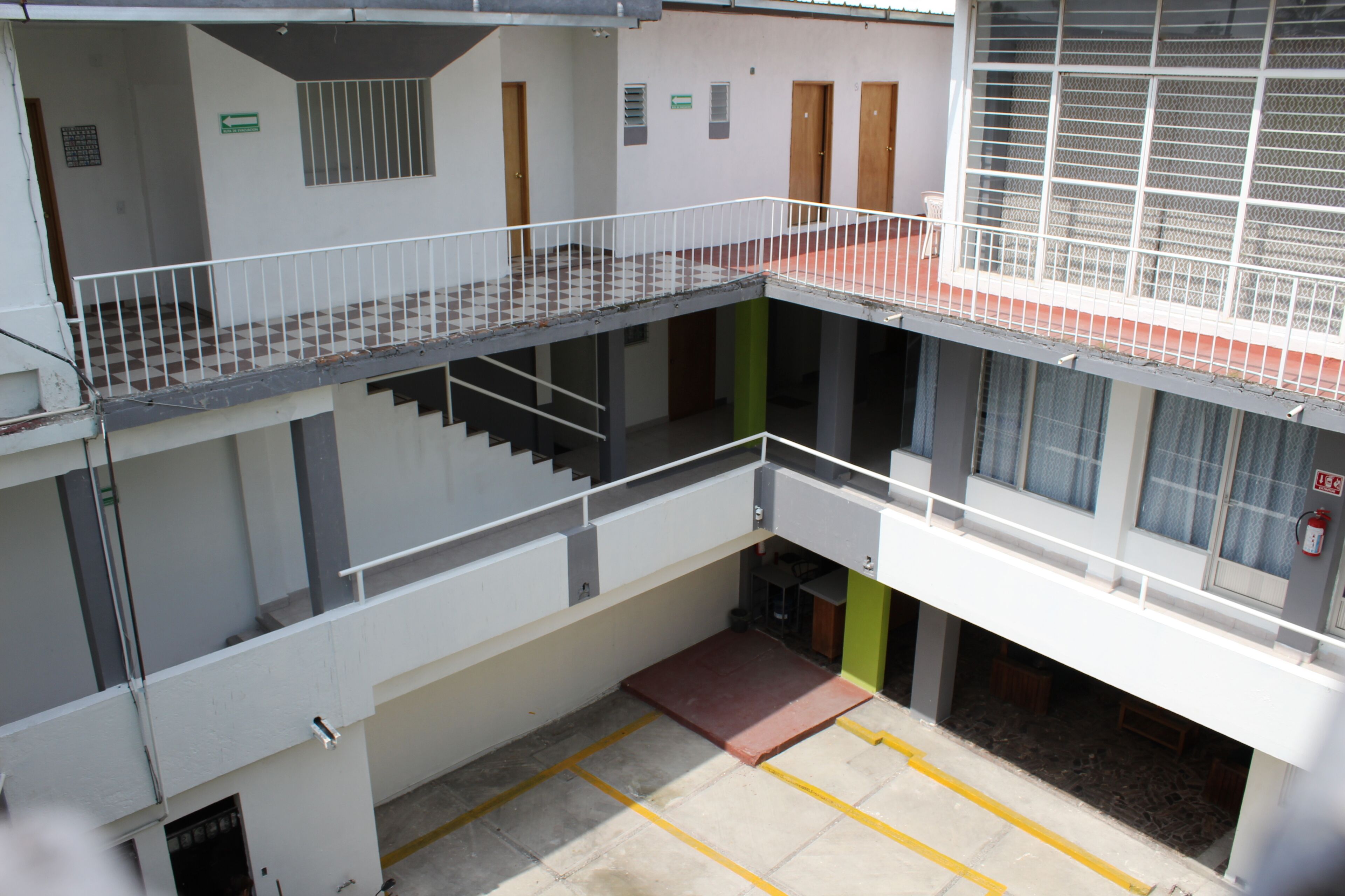 A multi-level building with a central staircase, a fire alarm, and a green door.