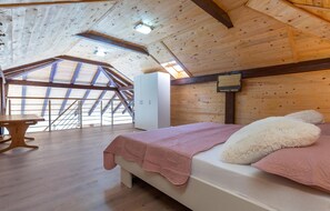 A bedroom with a sloped ceiling, wooden walls, a bed with a pink blanket, a white fluffy pillow, and a wooden table. - Amazing home in Lokvicici (Lokvicici)