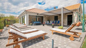 Un espacio al aire libre techado con sillones de sol, una hamaca y un edificio de piedra con techo de tejas.