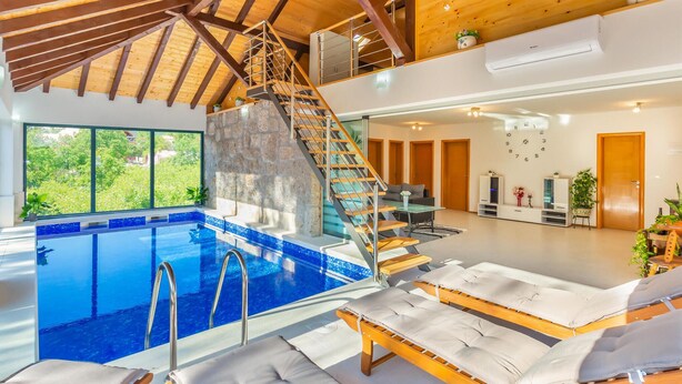 Una piscina interior amplia con una escalera de madera y sillones de descanso.