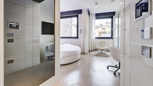 A modern bedroom with a bed, a chair, a desk, and a window with curtains.