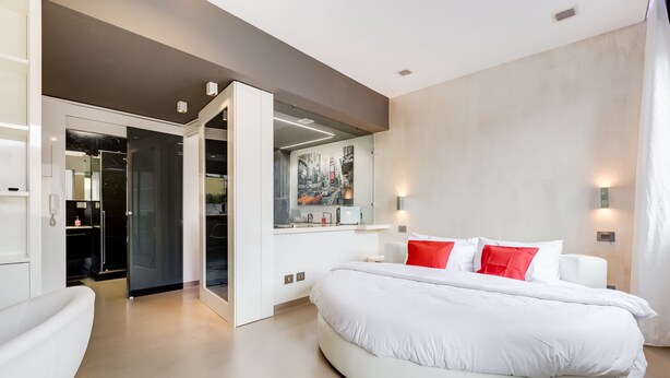 A modern bedroom with a circular bed, a walk-in closet, and a cityscape mural.