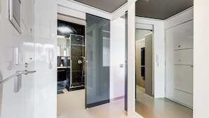 A modern hotel room with a large closet, a glass shower enclosure, and a visible bathroom.