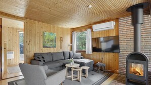 Un interno accogliente di una baita, con arredamento in legno, un divano, un tavolino, una TV e un camino.