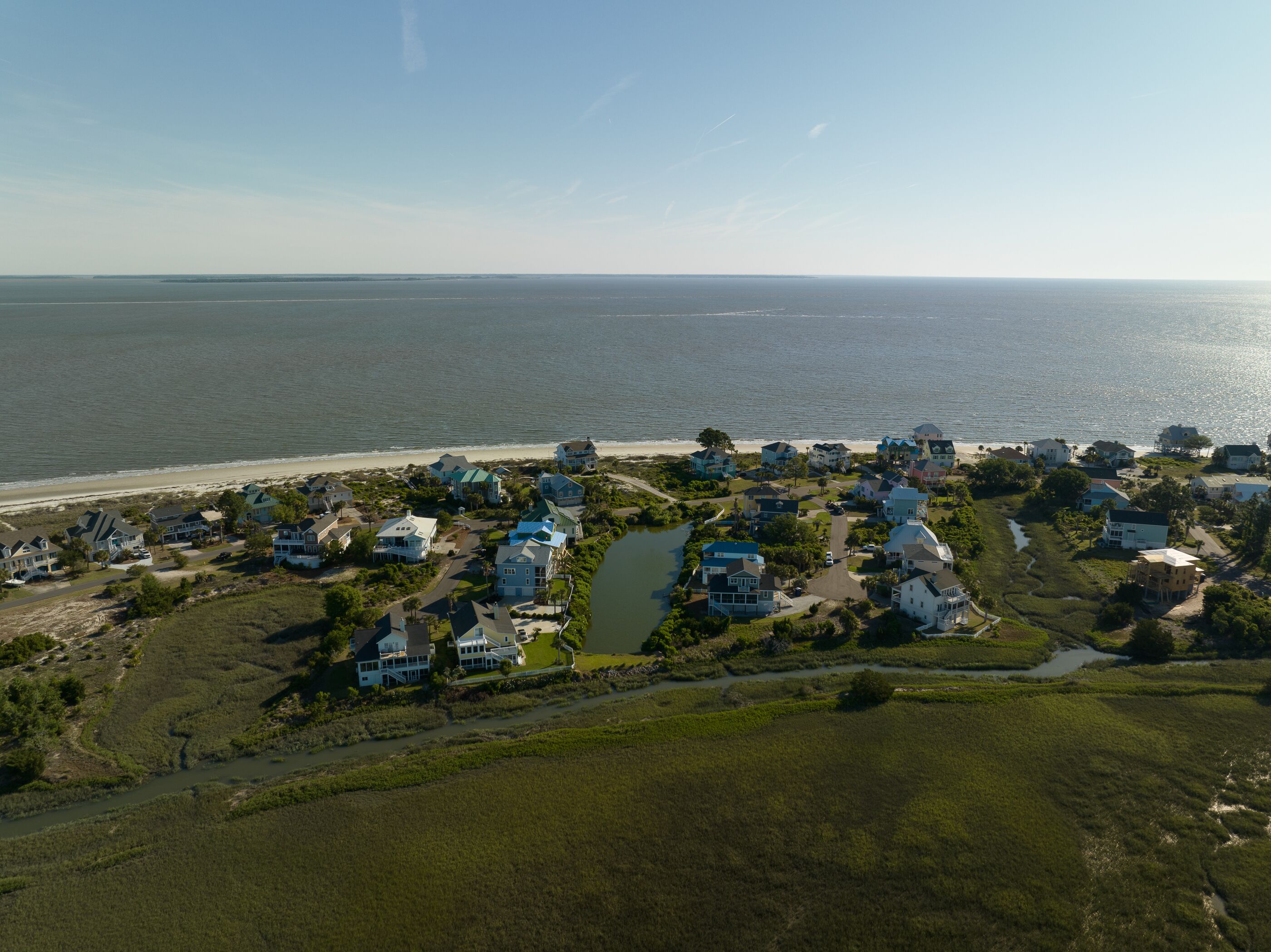 An aerial view of a coastal residential area with houses, a beach, and a river.