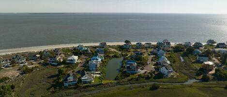 An aerial view of a coastal residential area with houses, a beach, and a river.