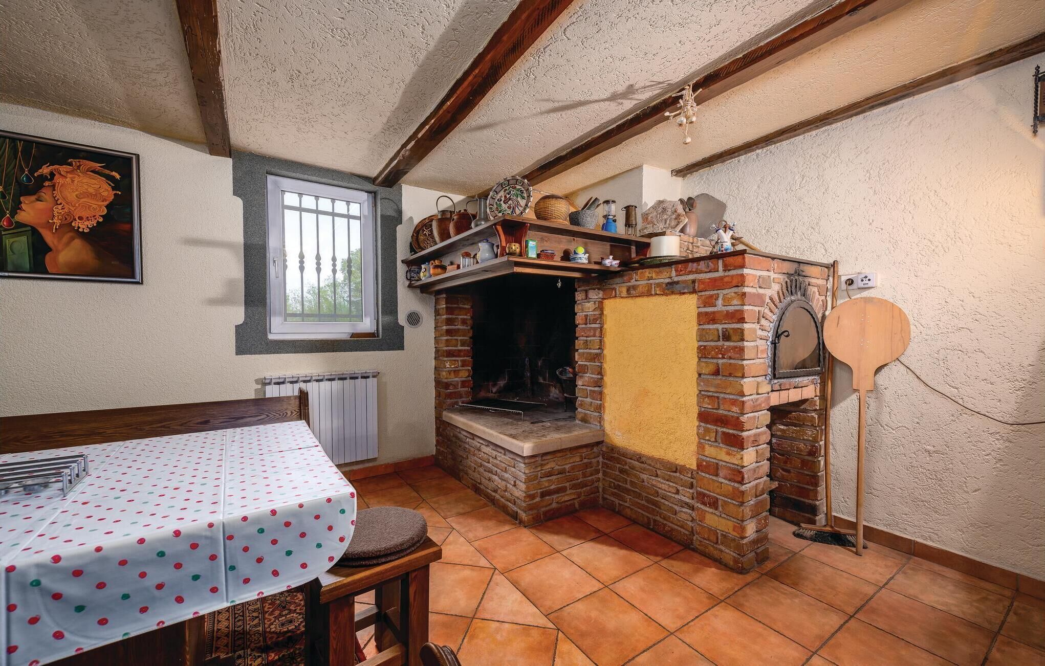 A rustic kitchen with a brick oven, a dining table with a polka dot tablecloth, and a window with bars.
