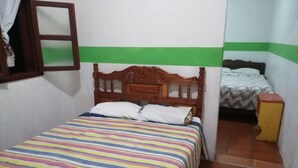 Un dormitorio con una cama de madera, una colcha a rayas de colores, una pared verde y blanca a rayas y una mesita de noche pequeña.