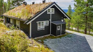 A dark wooden cabin with a sloped roof, a small attached shed, and a gravel driveway. - Lovely home in Rendalen with WiFi (Rendalen)
