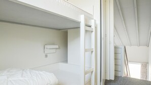 Quarto com beliche, parede branca, prateleira pequena e janela com cortinas.