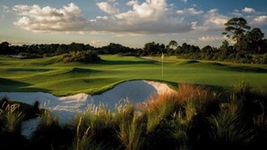 Campo de golf con un obstáculo acuático, árboles y cielo despejado.