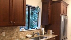 Una cocina con armarios de madera oscura, un refrigerador de acero inoxidable, una encimera de granito y un ventanal con vistas al verdor.