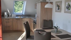 Een moderne keuken met houten kastjes, een eethoek met een tafel en stoelen, en een raam dat natuurlijk licht binnenlaat.