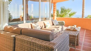 Un balcón soleado con mobiliario de mimbre, una mesa con bandeja y vistas al océano.