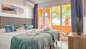 Habitación de hotel con dos camas, un ventanal con vistas a palmeras y un balcón con sillas.