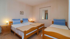 Una habitación con tres camas de madera, cada una con un colchón blanco y almohadas azules. Hay mesitas de noche con lámparas, un cuadro enmarcado en la pared y un espejo sobre las camas.