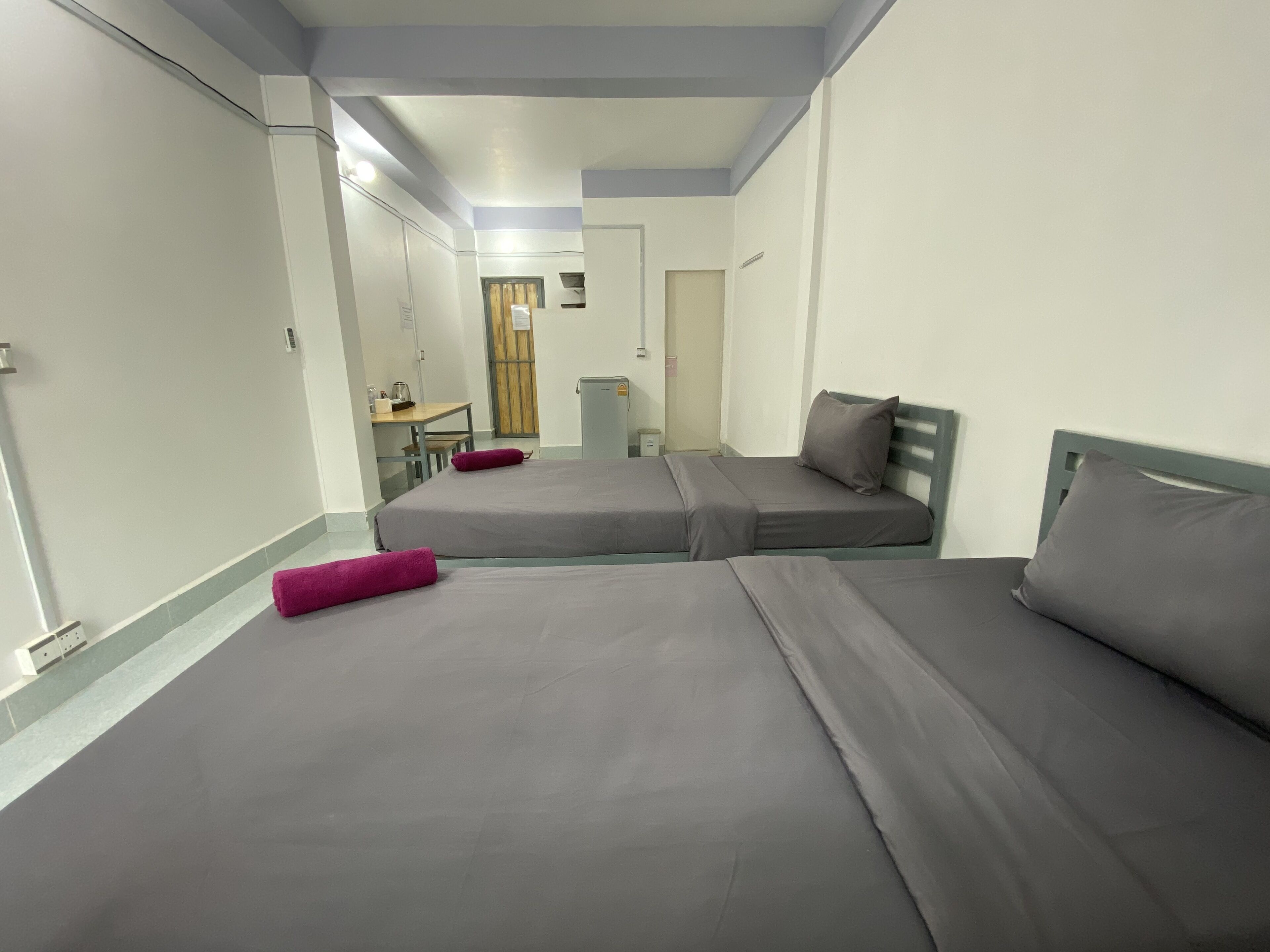 A room with two beds, a desk, and a small kitchenette.