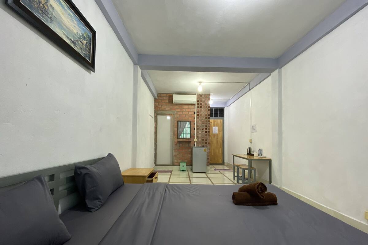 Une chambre d’hôtel comprenant un lit, une petite table, une chaise, un réfrigérateur et une porte donnant sur un couloir.