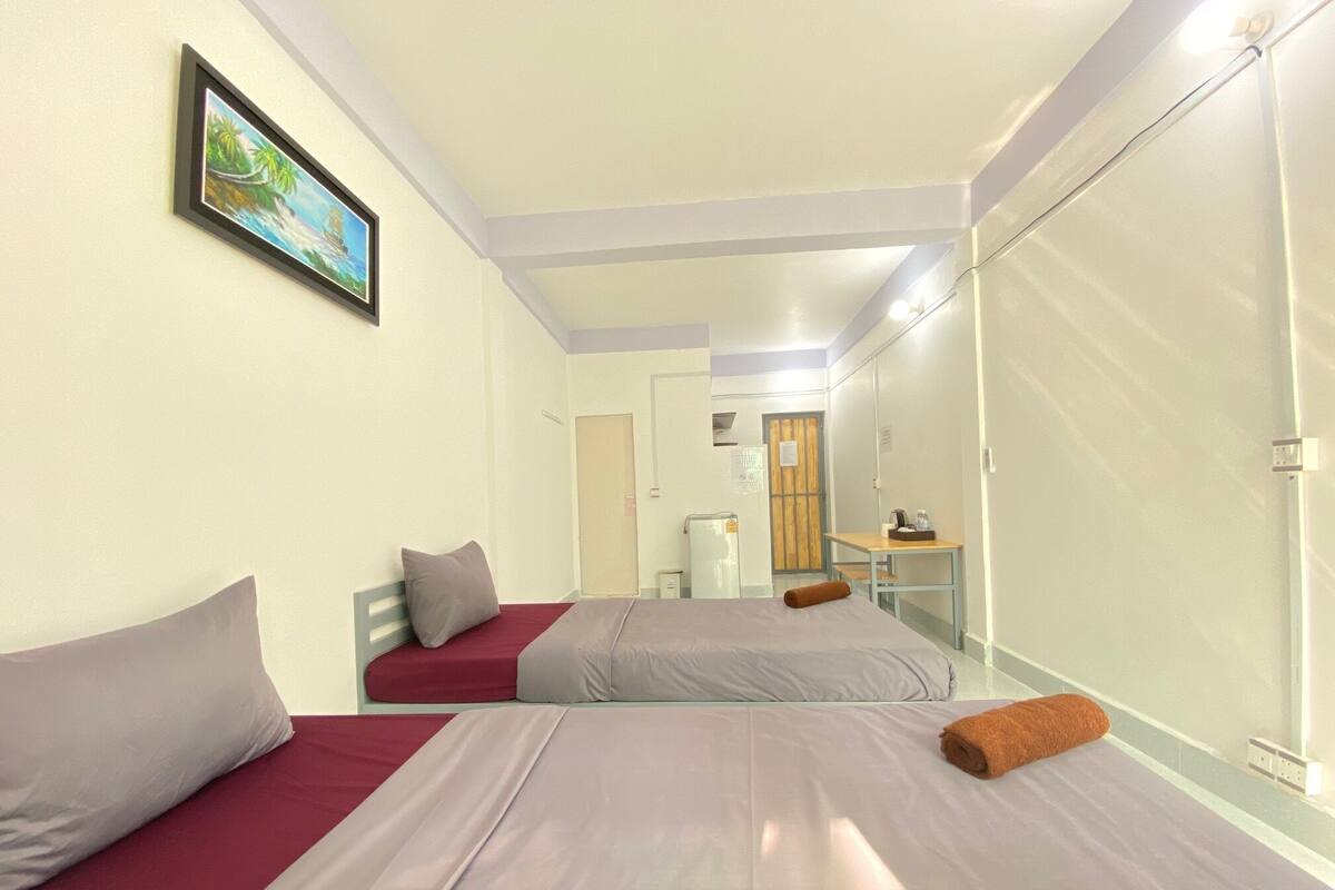 Une chambre d’hôtel avec deux lits, un petit bureau, un miroir et un tableau au mur.