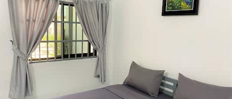 A room with a bed, grey curtains, a painting, and a window with bars.