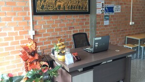 A reception desk with a laptop, a framed mural, and a brick wall. - Sevenstars Hostel (Sihanoukville)