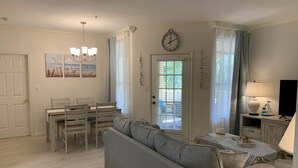 A living room with a grey sofa, dining table, chairs, a chandelier, a clock, and a television. - Luxury and charming 2Bdrm condo, minutes from beautiful Clearwater beach!  (Clearwater)
