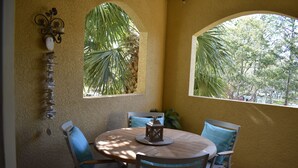 A round wooden table with four chairs, a decorative wall piece, and two windows with views of palm trees and a street. - Luxury and charming 2Bdrm condo, minutes from beautiful Clearwater beach!  (Clearwater)