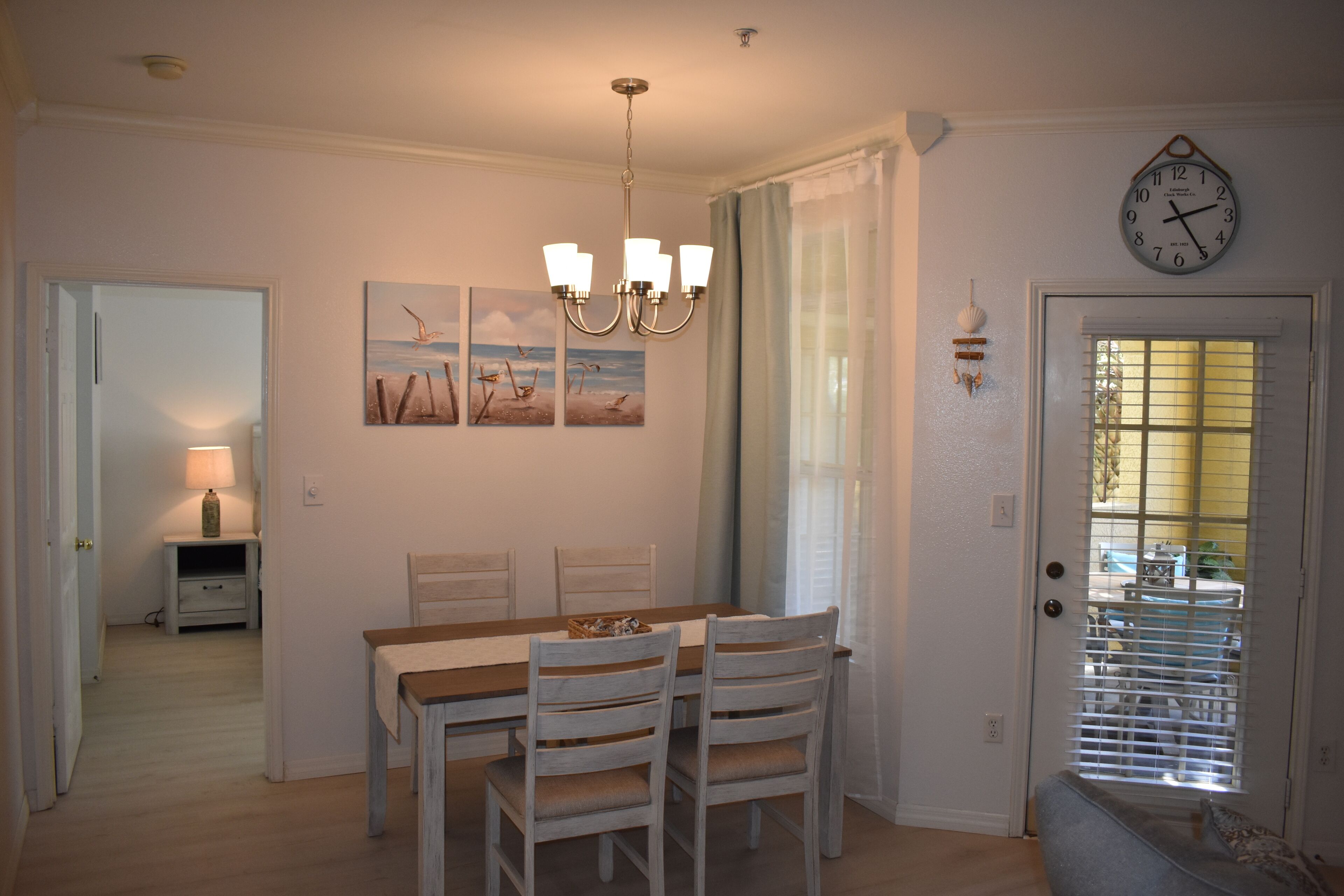 Un comedor con una mesa y sillas de madera, una araña y obras de arte en la pared.