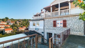 A two-story stone building with a balcony, a covered terrace, and a view of a hillside village. - Stunning apartment in Splitska (Splitska)