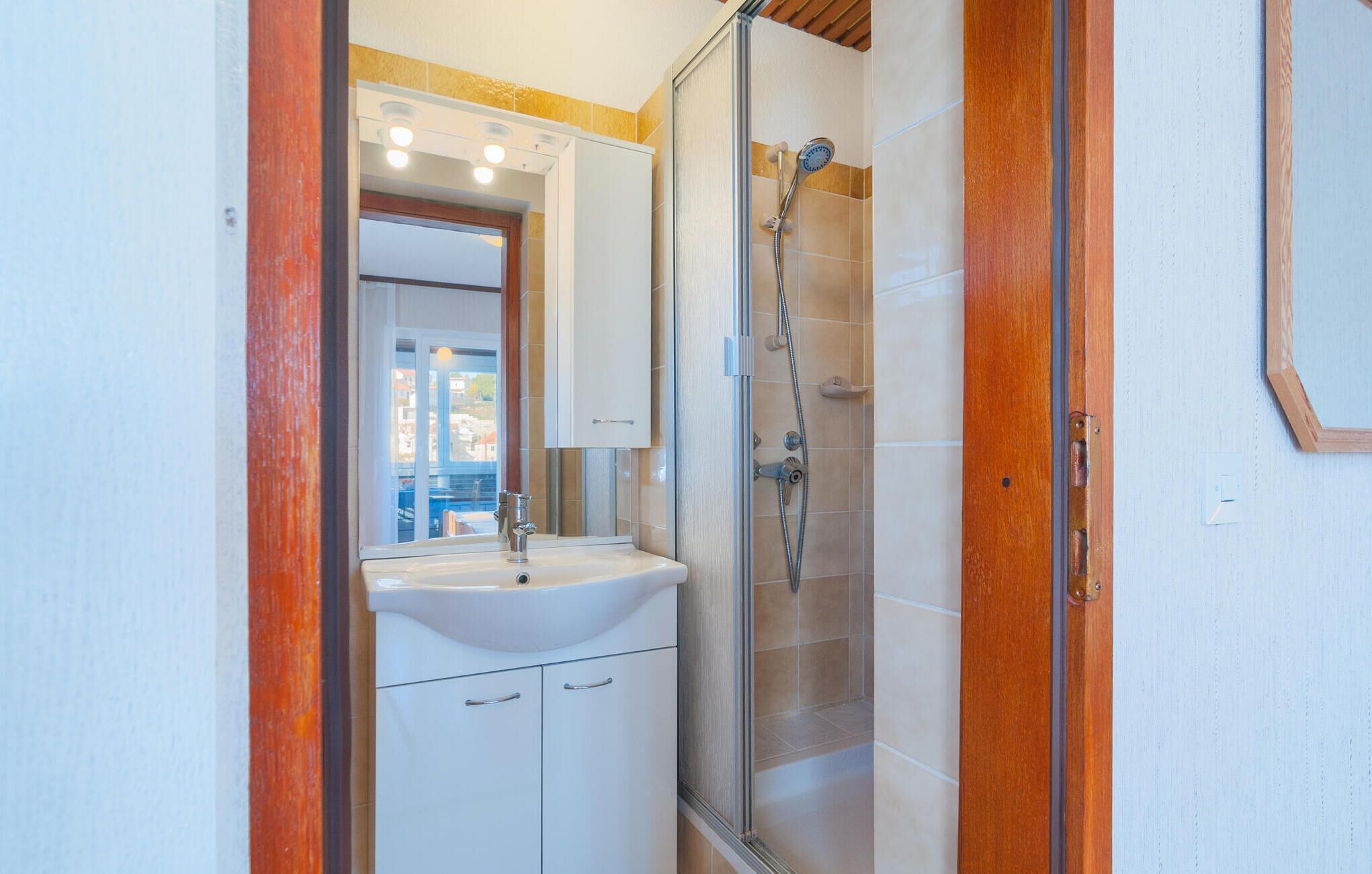 Un baño con lavamanos blanco, espejo y cabina de ducha con paredes de vidrio.