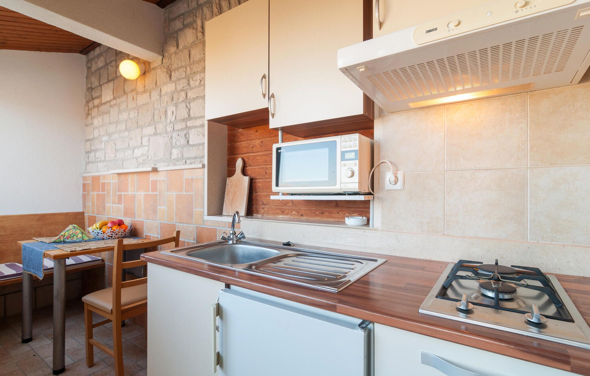 A compact kitchen with a gas stove, a microwave, a sink, and a wooden countertop.