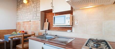 A compact kitchen with a gas stove, a microwave, a sink, and a wooden countertop.