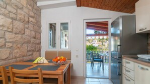 A kitchen with a stone wall, wooden dining table, and chairs. There is a view of a balcony with outdoor furniture. - Amazing apartment in Splitska (Splitska)