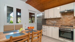 A modern kitchen with a wooden ceiling, white cabinets, a stainless steel refrigerator, a gas stove, and a window with a view of buildings. - Amazing apartment in Splitska (Splitska)