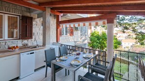 A balcony with a dining table set for four, surrounded by wicker chairs. A kitchen area with a sink and a dish rack is visible to the left. - Amazing apartment in Splitska (Splitska)