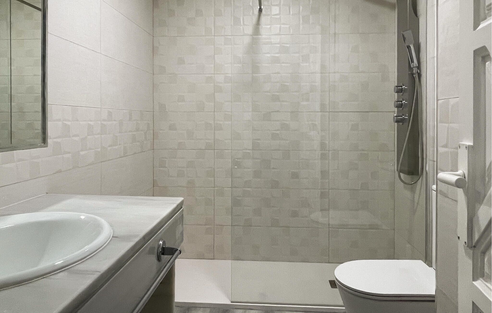 A small, tiled bathroom with a toilet, a sink, and a shower.