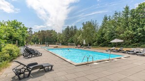 Une piscine rectangulaire dotée d’un plongeoir, entourée de chaises longues et de parasols.