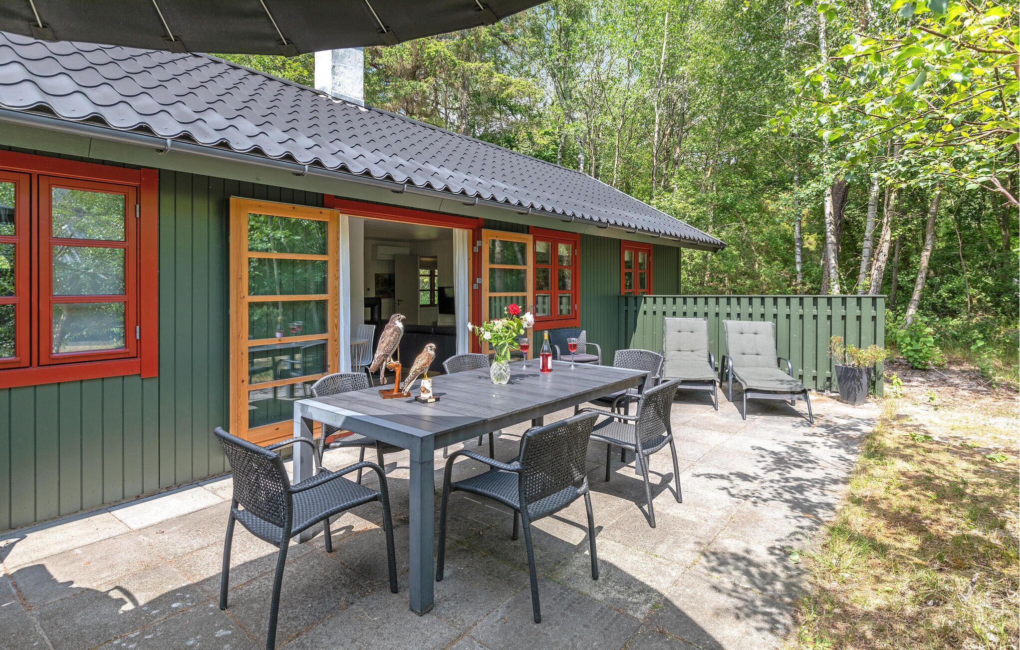Eine rustikale Holzhütte mit Essbereich, ausgestattet mit Tisch und Stühlen, umgeben von einer Holzterrasse und einem grünen Zaun.