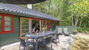 Un chalet rustique doté d’un coin repas avec une table et des chaises, entouré d’une terrasse en bois et d’une clôture verte.