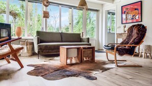 Una sala de estar moderna con un sofá, un sillón mullido, una mesa de centro de madera y un ventanal con vistas a la vegetación.