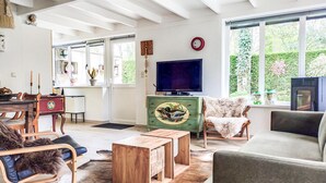 Sala de estar con televisor, muebles de madera, un mueble verde con diseño de pato y vistas al exterior.