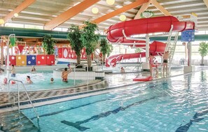 En indendørs swimmingpool med flere baner, en rød vandrutsjebane og et legeområde med farverige konstruktioner.